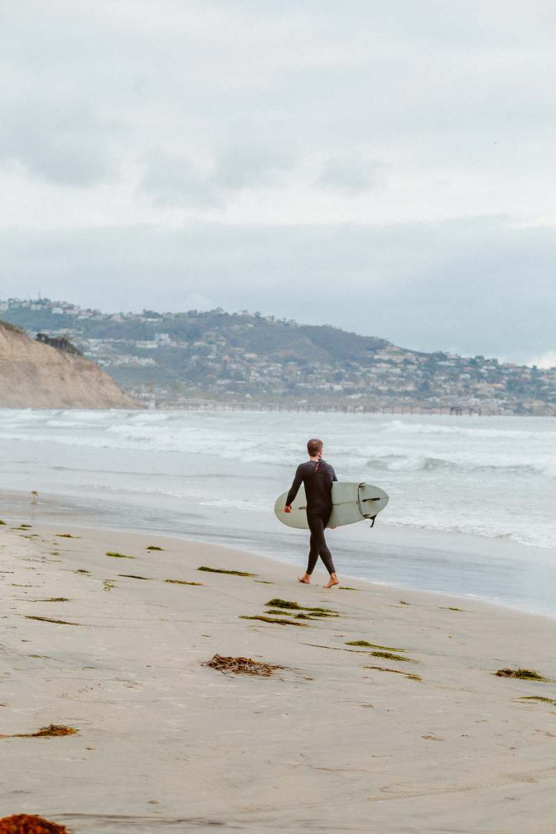 torrey pines man in black shorts carrying white surfboard walking on beach during daytime san diego